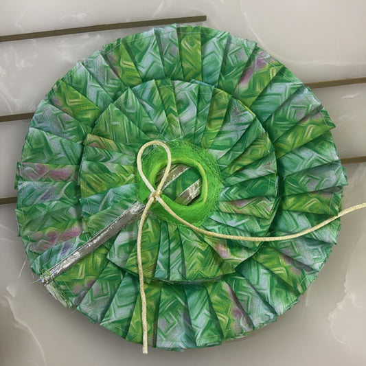 Green leaf-patterned fabric circle with a yellow thread on a white surface