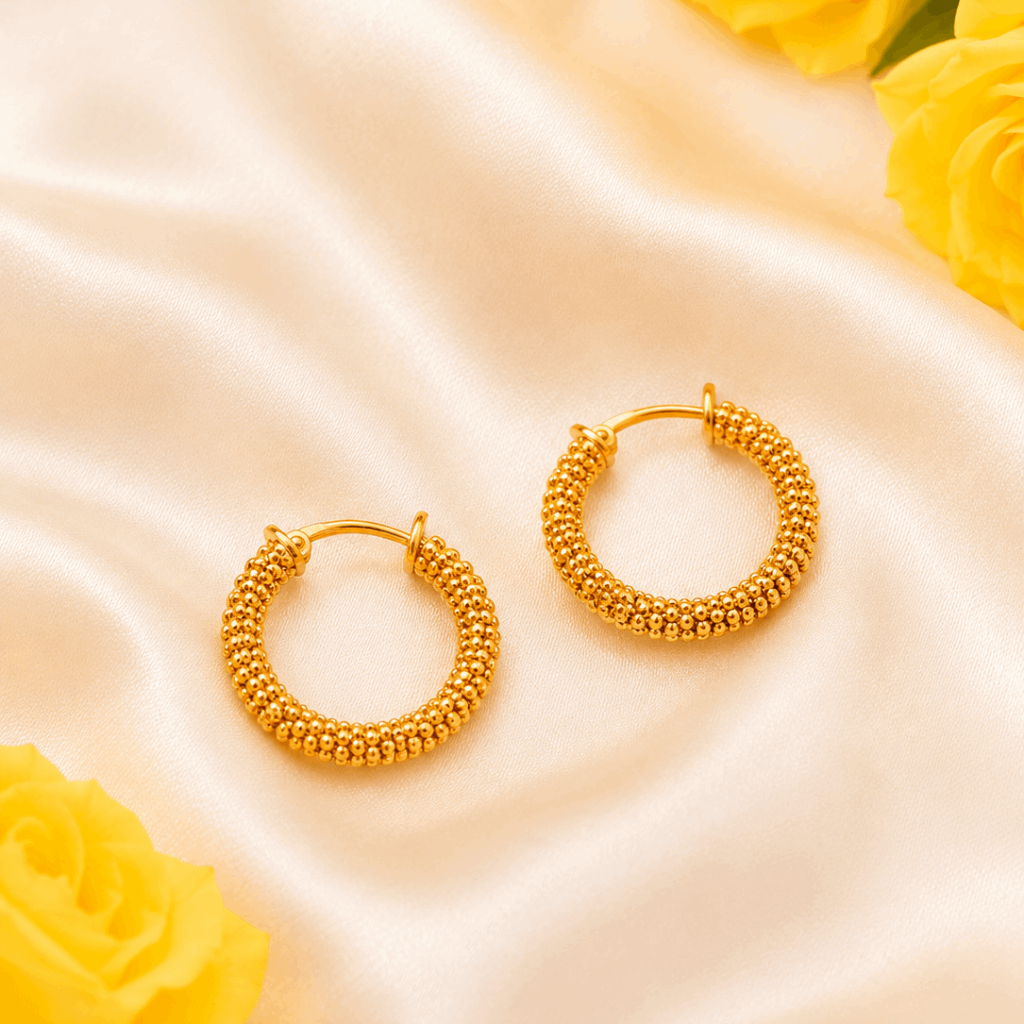 Gold hoop earrings on a satin surface with yellow roses.