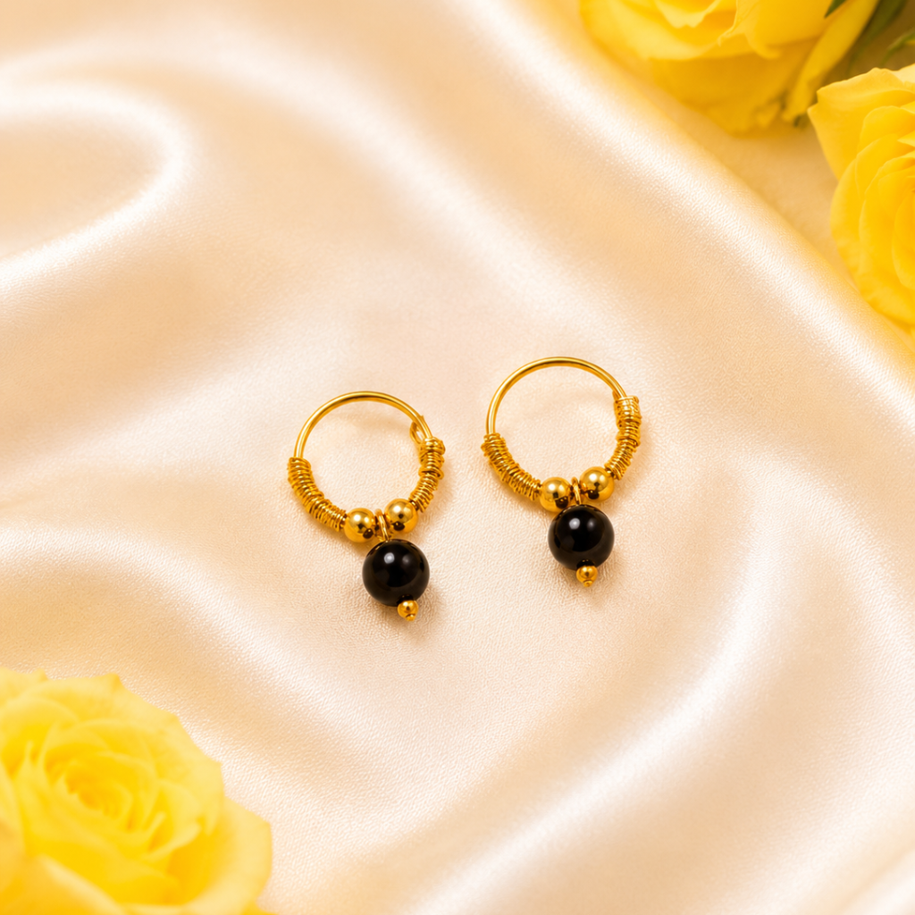 Gold hoop earrings with black beads on a satin surface with yellow roses.