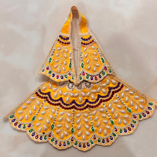 A yellow embroidered traditional garment or decorative textile piece with scalloped edges, mirror-like embellishments, and colorful bead accents, photographed against a light beige background.