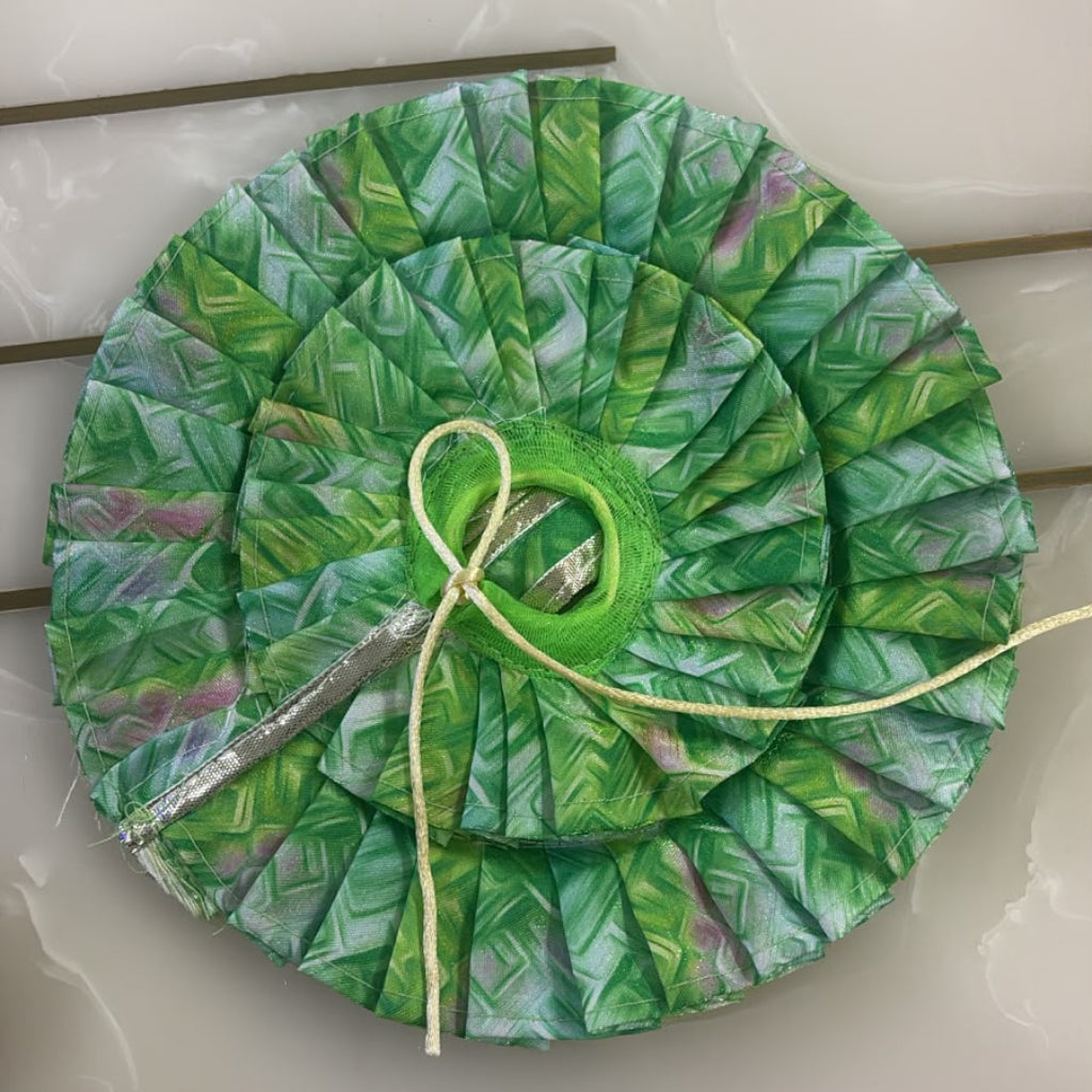 Green leaf-patterned fabric circle with a yellow thread on a white surface