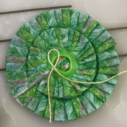 Green leaf-patterned fabric circle with a yellow thread on a white surface