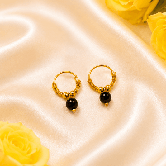 Gold hoop earrings with black beads on a satin surface with yellow roses.