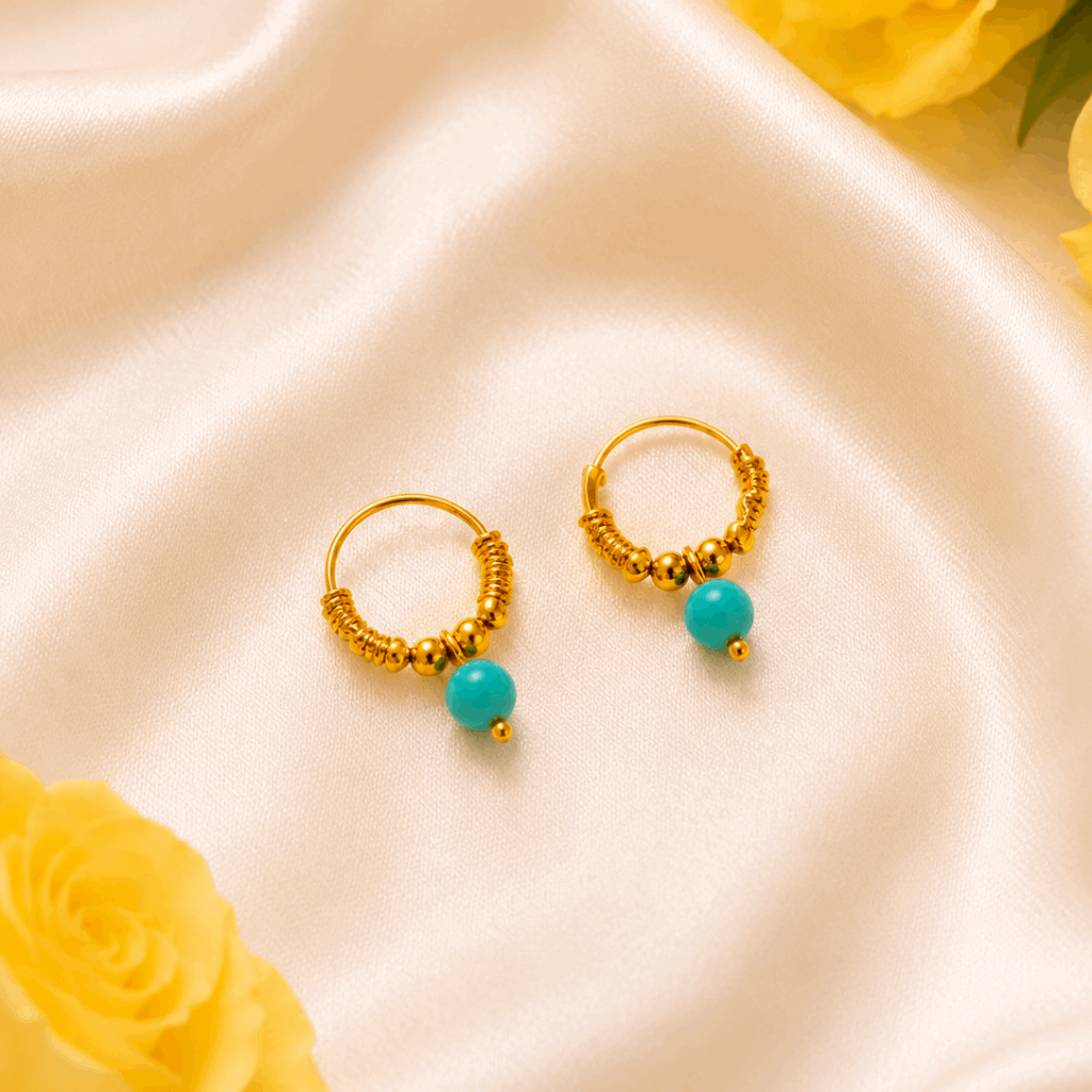 Gold hoop earrings with turquoise beads on a satin surface with yellow roses.