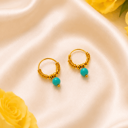 Gold hoop earrings with turquoise beads on a satin surface with yellow roses.