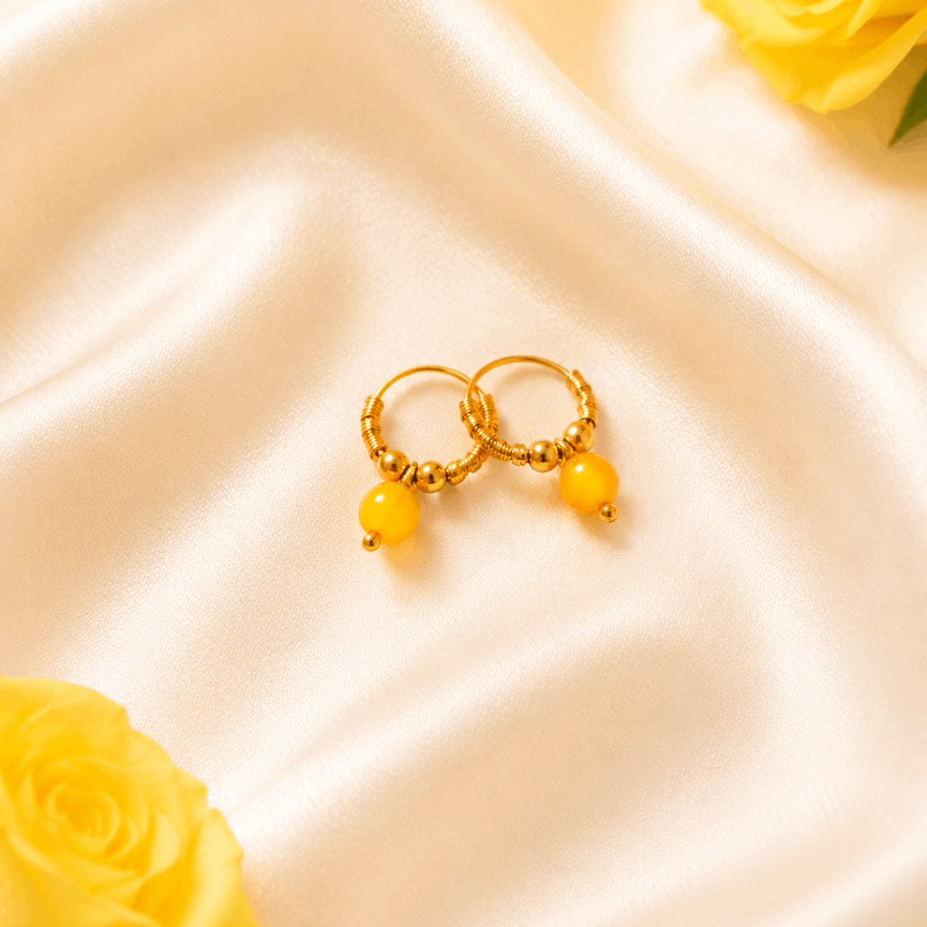 Gold hoop earrings with yellow beads on a satin surface with yellow roses.