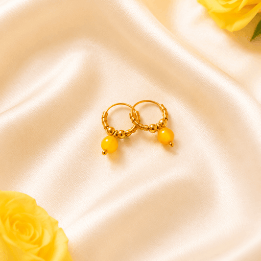 Gold hoop earrings with yellow beads on a satin surface with yellow roses.