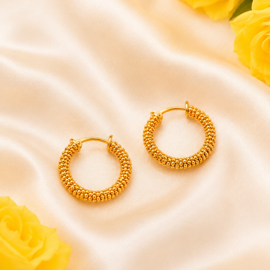 Gold hoop earrings on a satin surface with yellow roses.