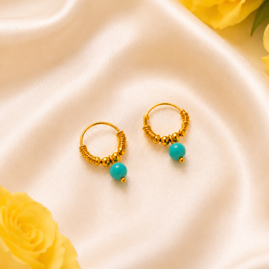 Gold hoop earrings with turquoise beads on a satin surface with yellow roses.