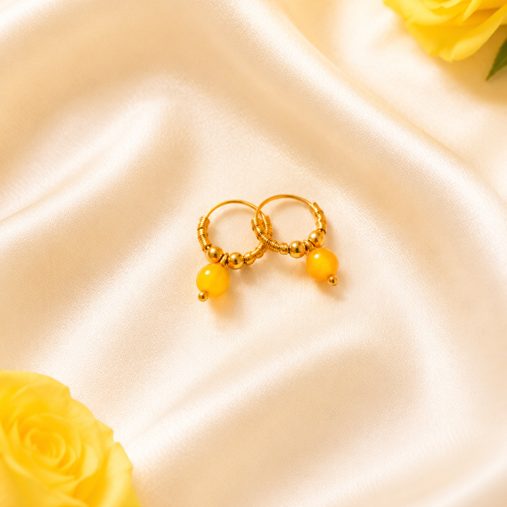 Gold hoop earrings with yellow beads on a satin surface with yellow roses.