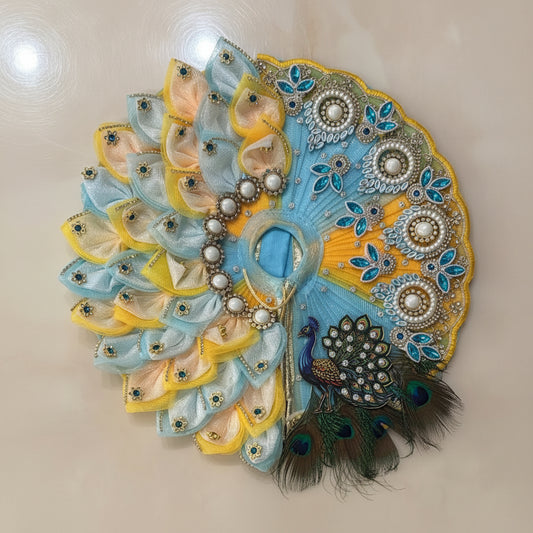 Handcrafted peacock-themed designer dress and matching crown for Ladoo Gopal Ji, featuring blue and yellow petal layers and teal crystal accents.