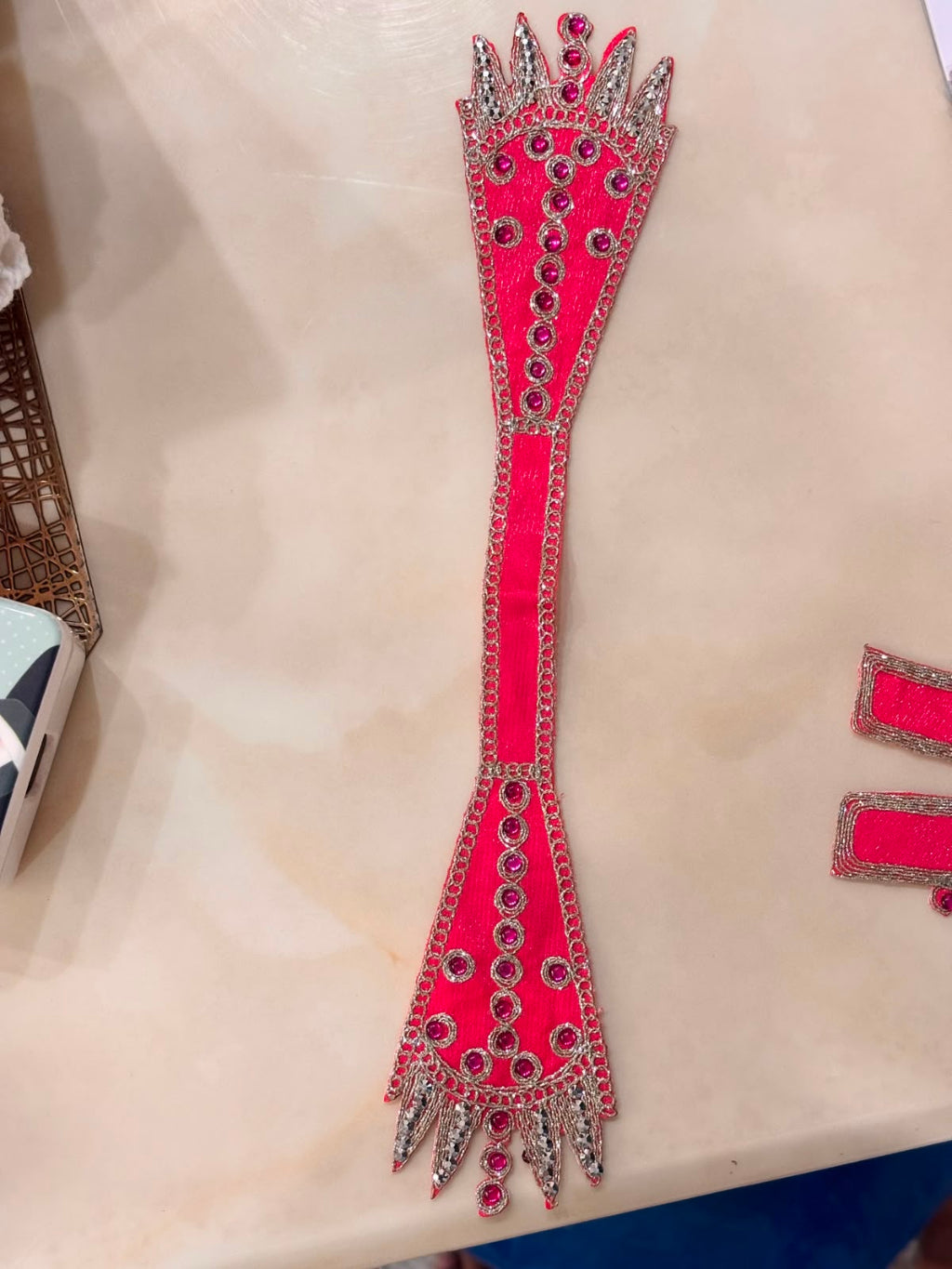 A bright pink traditional embroidered garment piece with silver mirror-work and red sequins, laid flat on a beige surface.