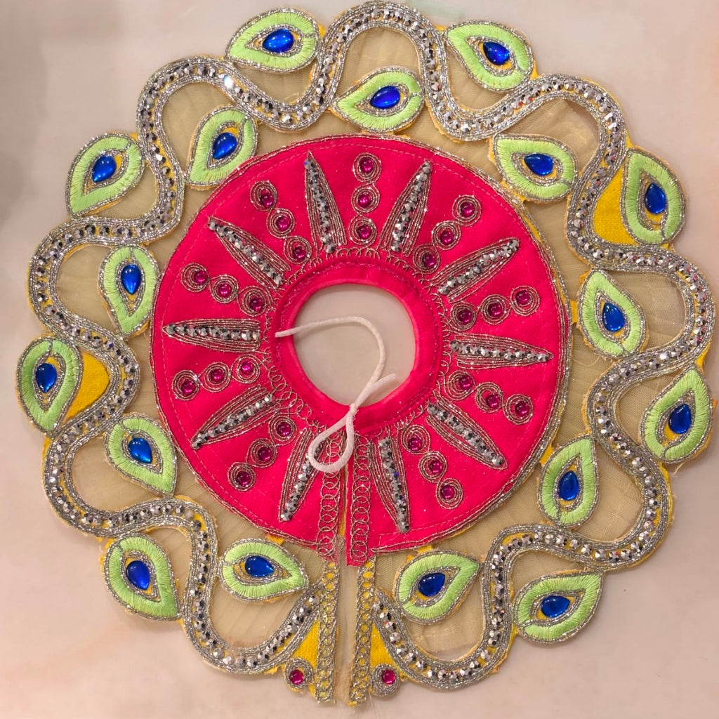 Handcrafted fuchsia pink designer dress and matching yellow crown for Ladoo Gopal Ji, featuring peacock-plume borders and blue gemstone accents.