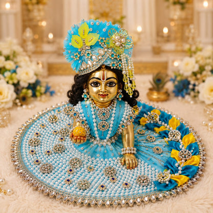 Handcrafted sky-blue and yellow designer dress and matching crown for Ladoo Gopal Ji, featuring pearl work and intricate petal detailing.