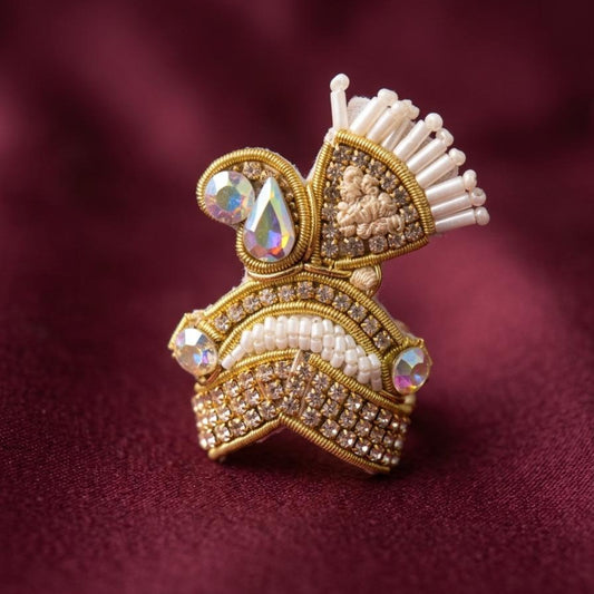 Handcrafted gold and pearl designer mukut for Ladoo Gopal Ji with iridescent stone detailing.