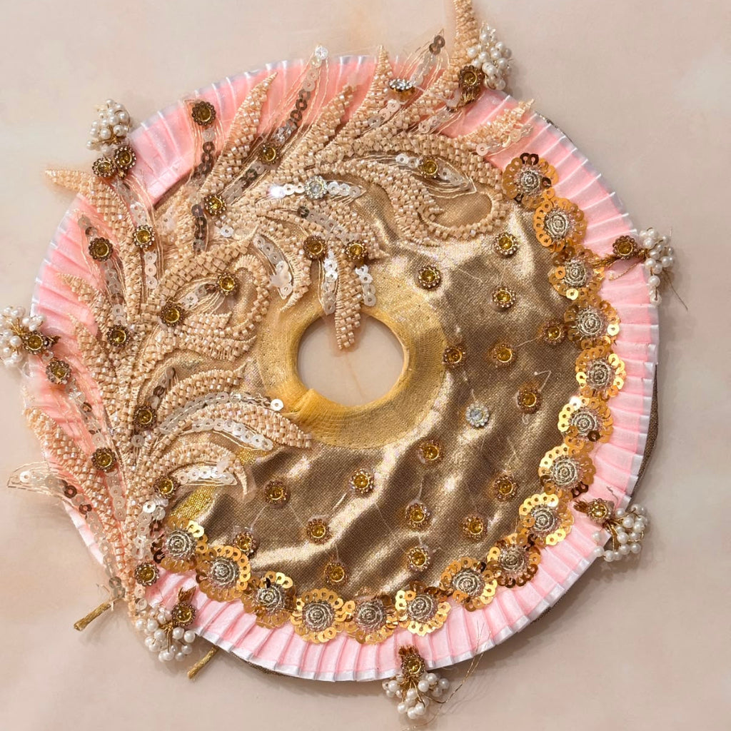 Handcrafted champagne gold and soft pink designer dress and matching crown for Ladoo Gopal Ji, featuring metallic embroidery and pearl detailing.