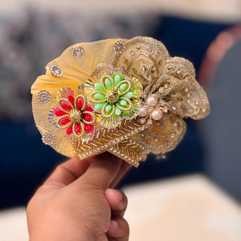 Handcrafted golden beaded designer dress and matching crown for Ladoo Gopal Ji, featuring silver floral borders and vibrant stone accents.