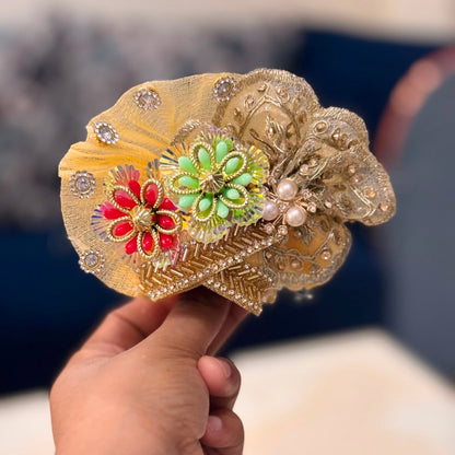 Handcrafted golden beaded designer dress and matching crown for Ladoo Gopal Ji, featuring silver floral borders and vibrant stone accents.