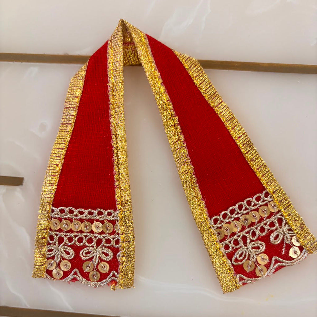 A red velvet scarf with ornate gold and silver embroidery and mirror work, displayed on a light marble surface.